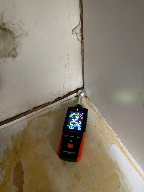 Laserline meter (orange/black) at a water-stained wall corner